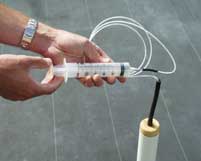 Syringe with small clear tube that traverses black tube. Clear tube extends to bottom of lysimeter